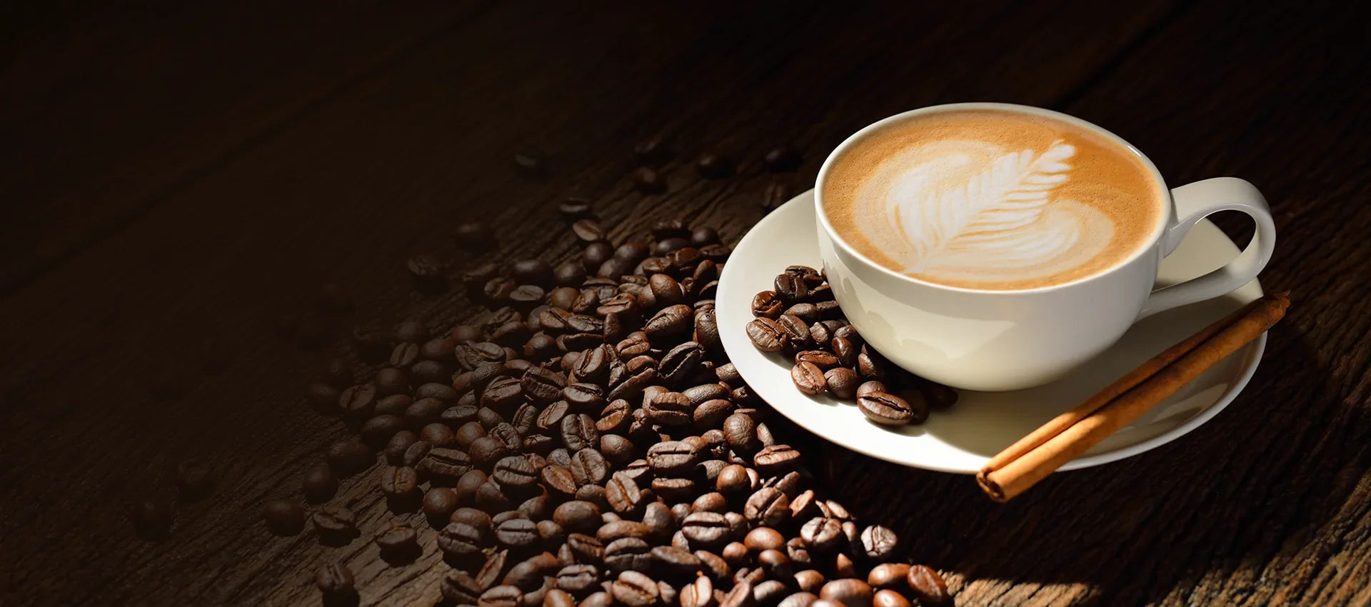 Cup of coffee with latte art on a wooden surface with coffee beans and cinnamon sticks.