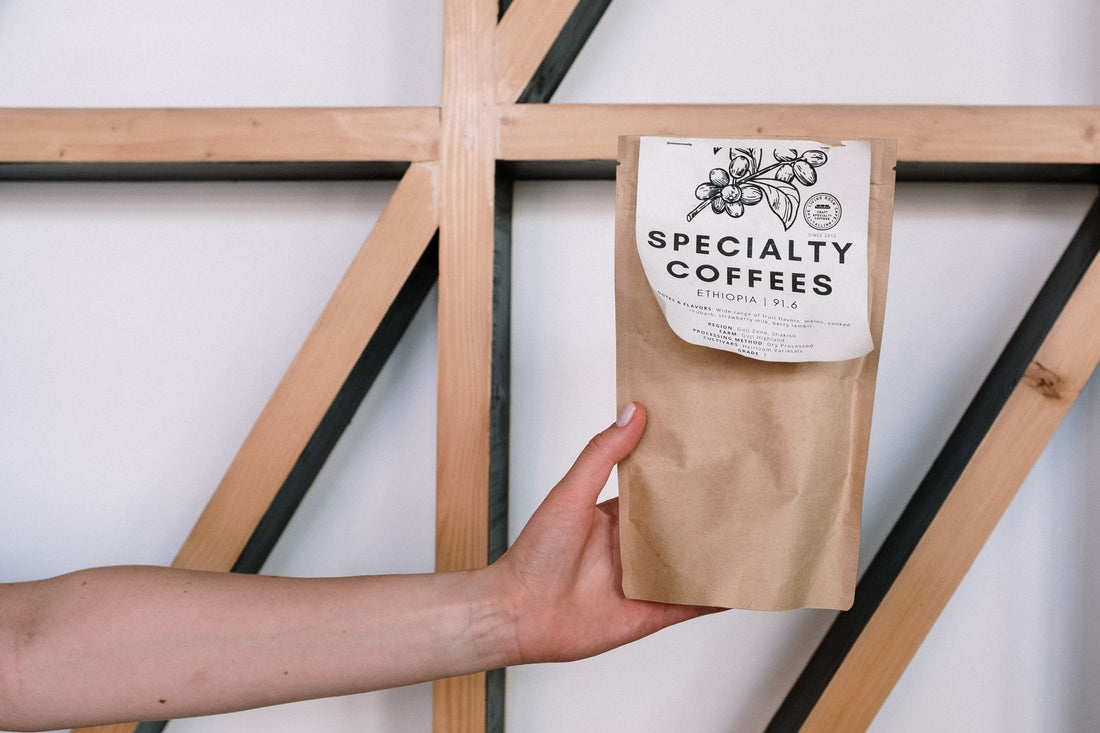 A hand holding a specialty coffee package against a minimalist background with wooden beams.