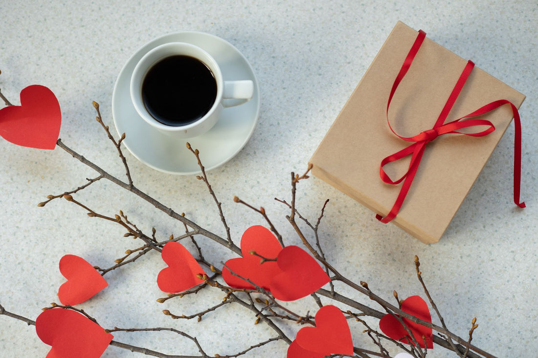 Top view of paper hearts on twigs near gift in craft paper and cup of coffee on table