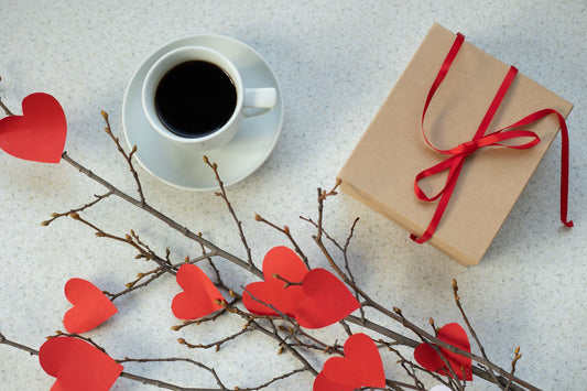 Top view of paper hearts on twigs near gift in craft paper and cup of coffee on table