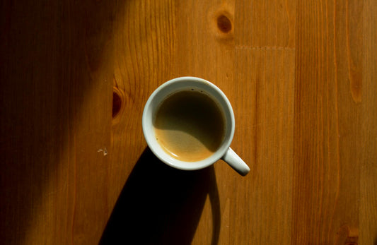 A simple, minimalist approach capturing a cup of coffee casting a shadow on a wooden table.