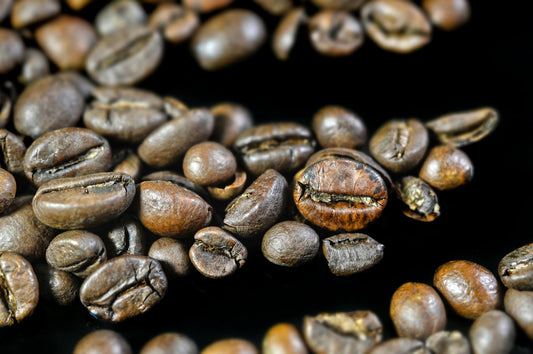 Detailed close-up image of aromatic roasted coffee beans scattered on a black surface.