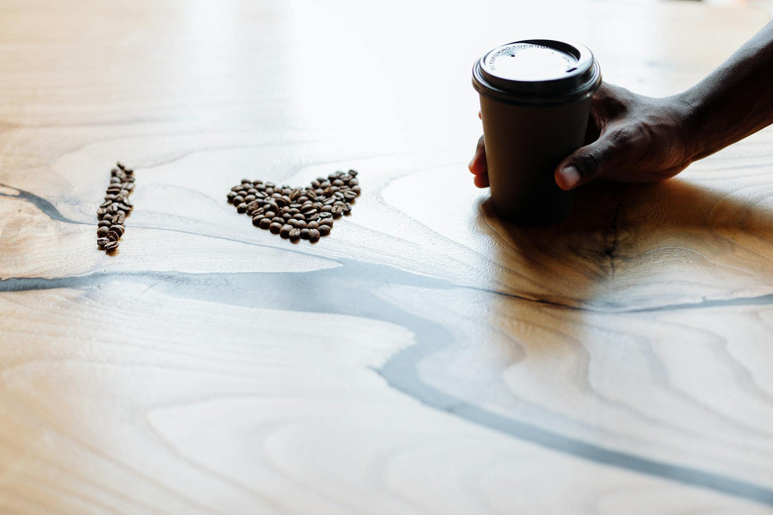 Coffee beans forming love shape on wooden table with hand holding a cup creating a warm, inviting scene.