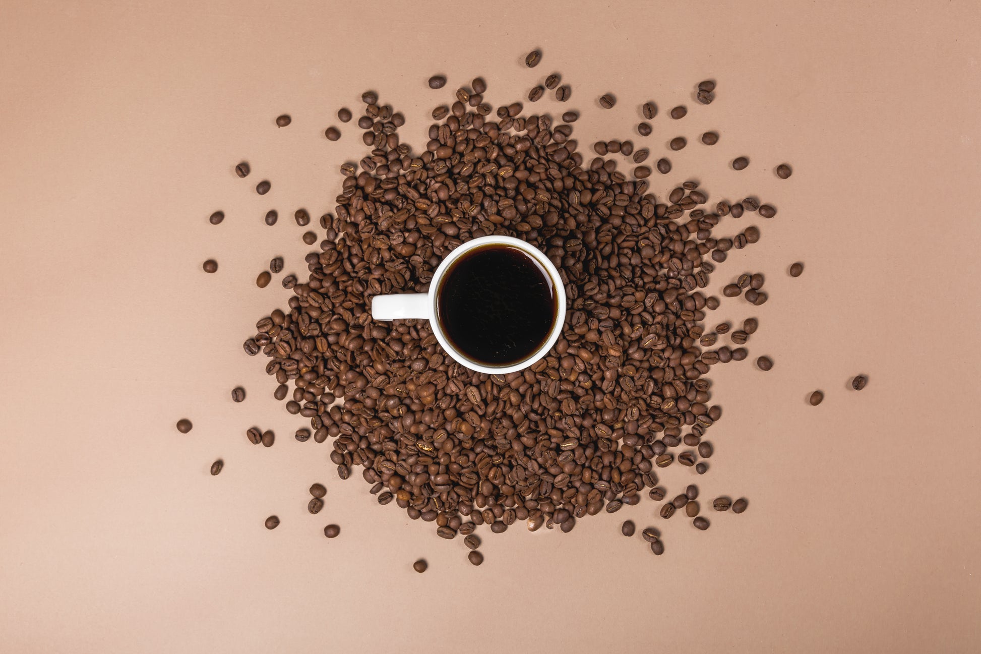 Cup of black coffee surrounded by roasted coffee beans representing UfuKoffee medium-dark roast coffee pods